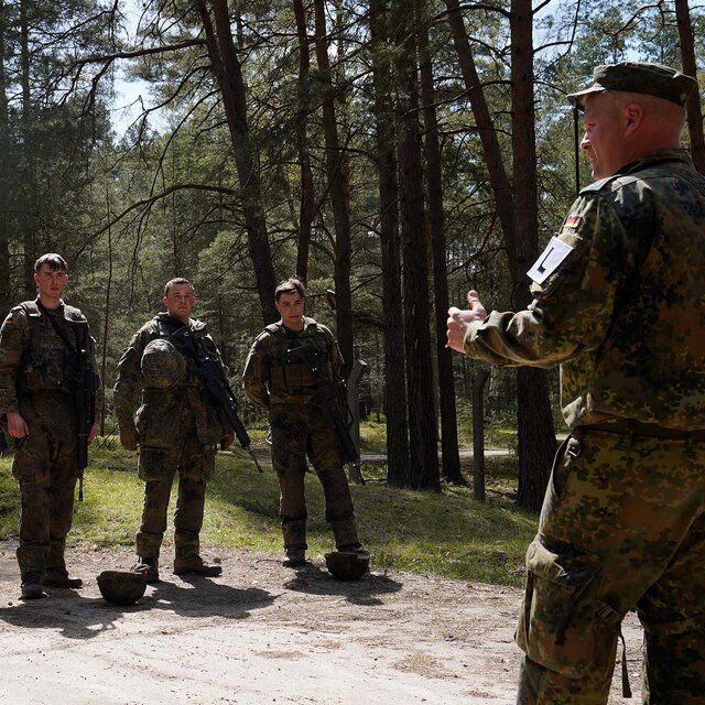 Drei auszubildende Soldaten in Uniform stehen mit ihrem Ausbilder in einem Wald