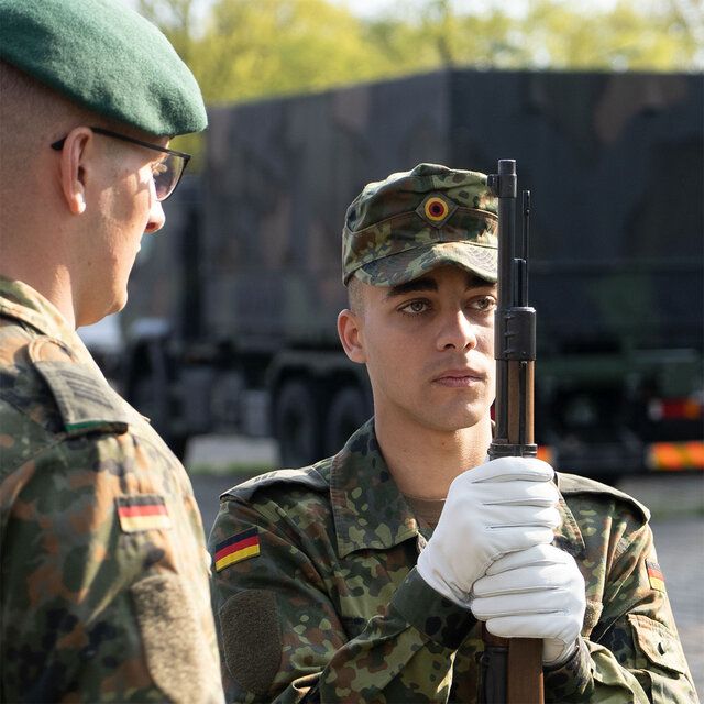 Ein Soldat während seiner Ausbildung zum Protokollsoldaten mit einem Gewehr und einem Ausbilder