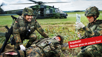 Eine Soldatin und ein Soldat der Bundeswehr leisten erste Hilfe bei einem verwundeten Kameraden. Im Hintergrund ist ein Hubschrauber zu sehen. Der Hinweistext "Ausgebucht! Besuche gerne ein anderes Event" ist zu sehen.