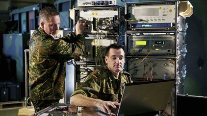 2 Soldaten der Bundewehr im IT-Bataillon arbeiten an einem Laptop der mit einem Server verbunden ist.