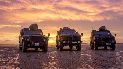 3 Fahrzeuge der Bundeswehr stehen beim Sonnenuntergang an einem Strand 