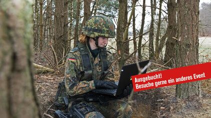 Eine Soldatin kniet mit einem Laptop in einem Wald.