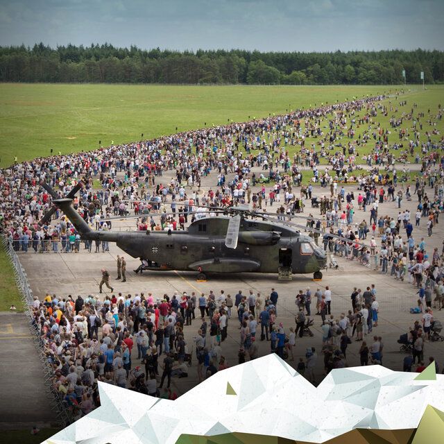 Ein Bundeswehr Hubschrauber steht auf einem Flugplatz. Drumherum sind hunderte Menschen zu sehen.