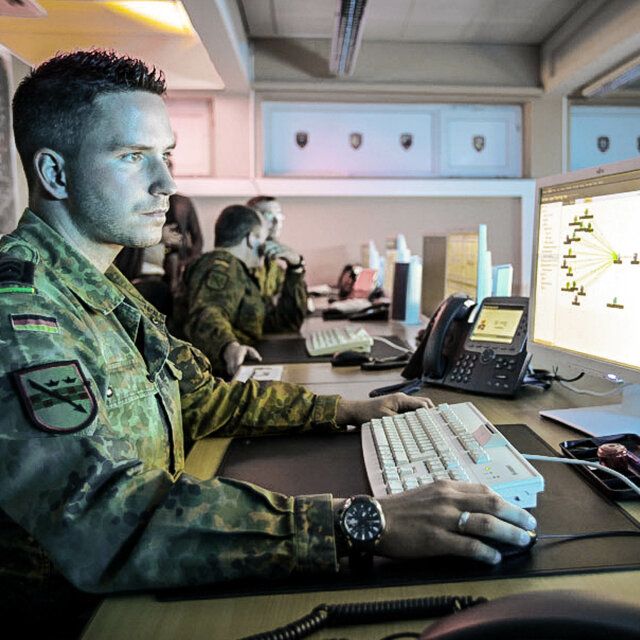 3 Soldaten in Uniform befinden sich in einem Büro und arbeiten an ihren Computern. 