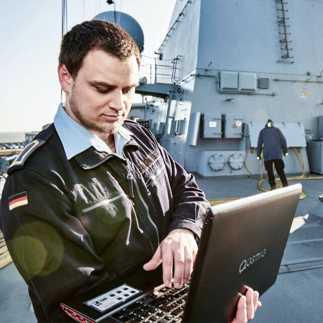 Ein Marine Soldat bedient einen Laptop an Deck eines Bundeswehrschiffes.