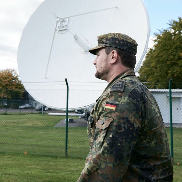 Ein Soldat ist vor einer groÃŸen SatellitenschÃ¼ssel zu sehen. 