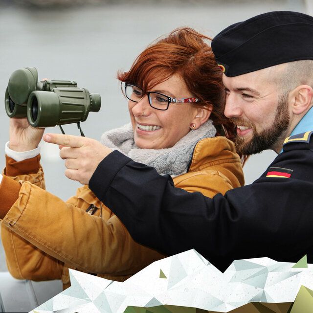 Ein Marine Soldat zeigt einer Frau etwas durch ein Fernglas.