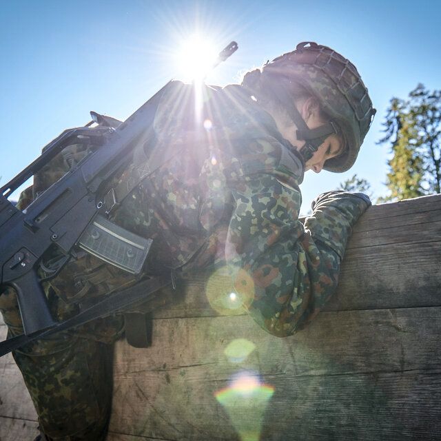 Eine Soldatin Ã¼berwindet eine Hinderniswand mit ihrer AusrÃ¼stung und dem Gewehr G36.