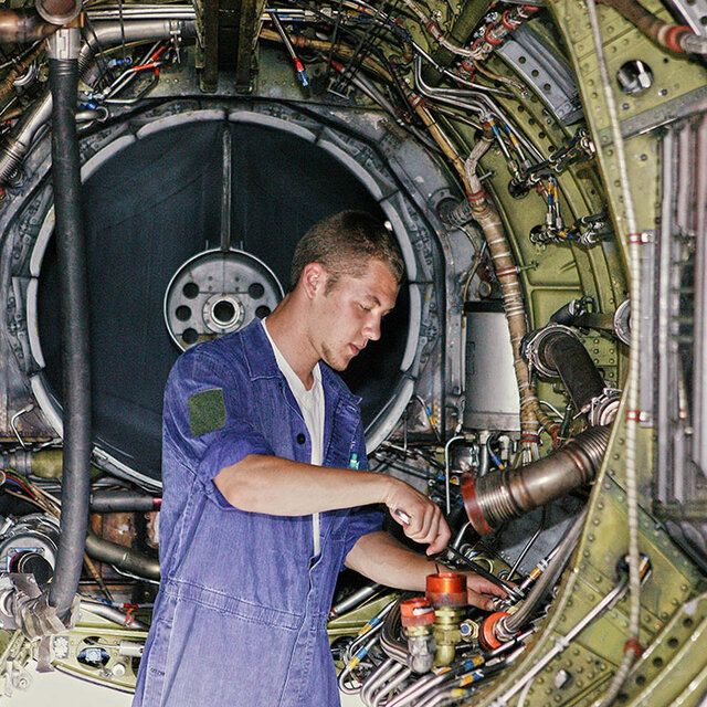 Ein Techniker in einem blauen Arbeitsoverall kontrolliert die Technik beim Eurofighter. 