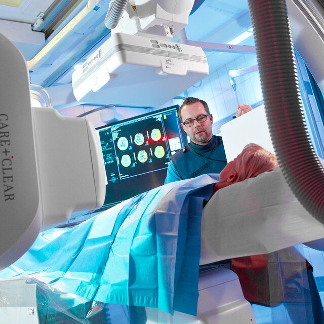 Eine Patientin liegt unter einem Röntgengerät während sich ein Arzt mit ihr unterhält. 