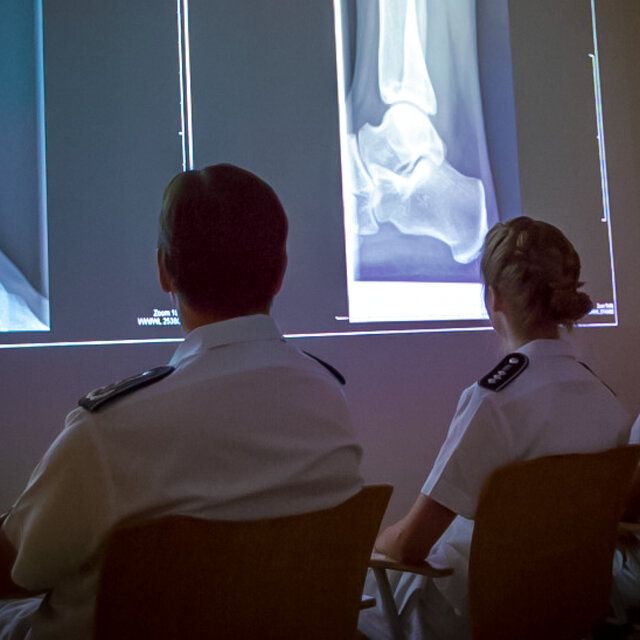 Eine Ã„rztin und ein Arzt der Bundeswehr nehmen an einer medizinischen Weiterbildung teil. RÃ¶ntgenbilder werden an einer Wand dargestellt.  