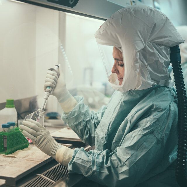 Eine Frau in einem Schutzanzug entnimmt Proben in einem Labor. 