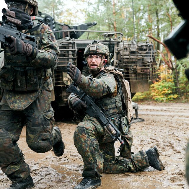 Soldat_innen dringen in Richtung Wald vor. Ein Soldat zeigt die vorgegebene Richtung an.