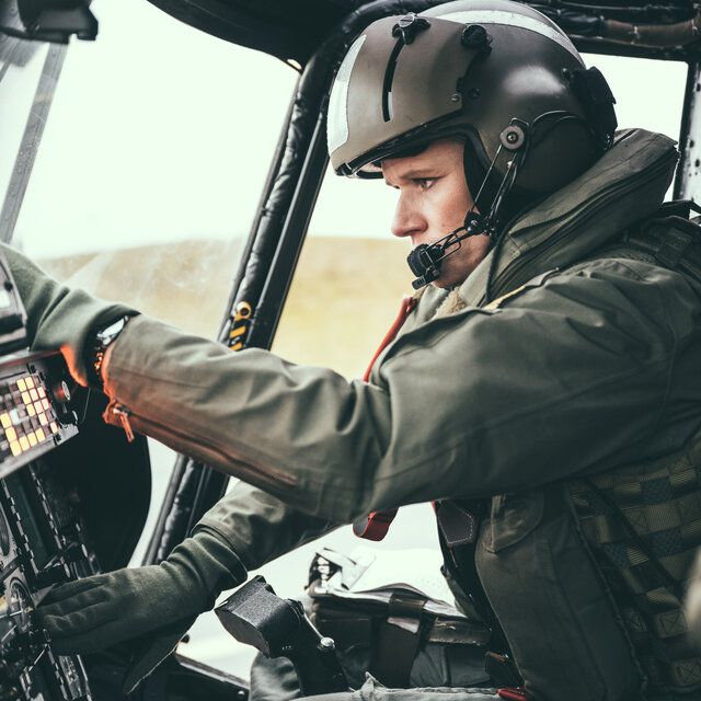 Ein Pilot sitzt im Cockpit eines Hubschraubers und stellt etwas an seinem Display ein.