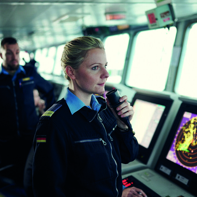 Eine Offizierin der Marine befindet sich im Navigationsraum des Schiffes und gibt Anweisungen an die Besatzung weiter.