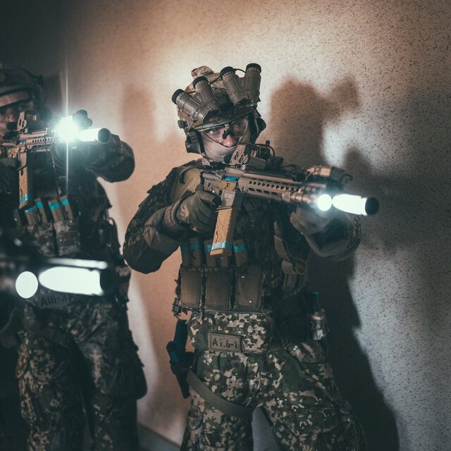 Soldaten der SpezialkrÃ¤fte bewegen sich mit Gewehren mit eingebauten Taschenlampen auf ein GebÃ¤ude zu.