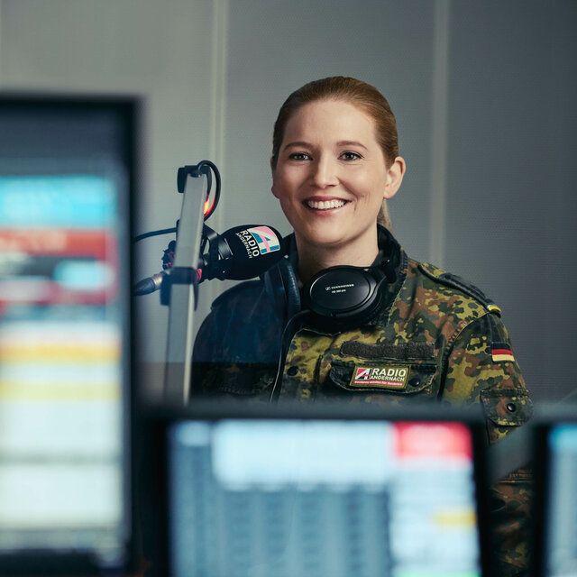Eine Bundeswehr Soldatin steht mit Headset vor einem Mikrofon.